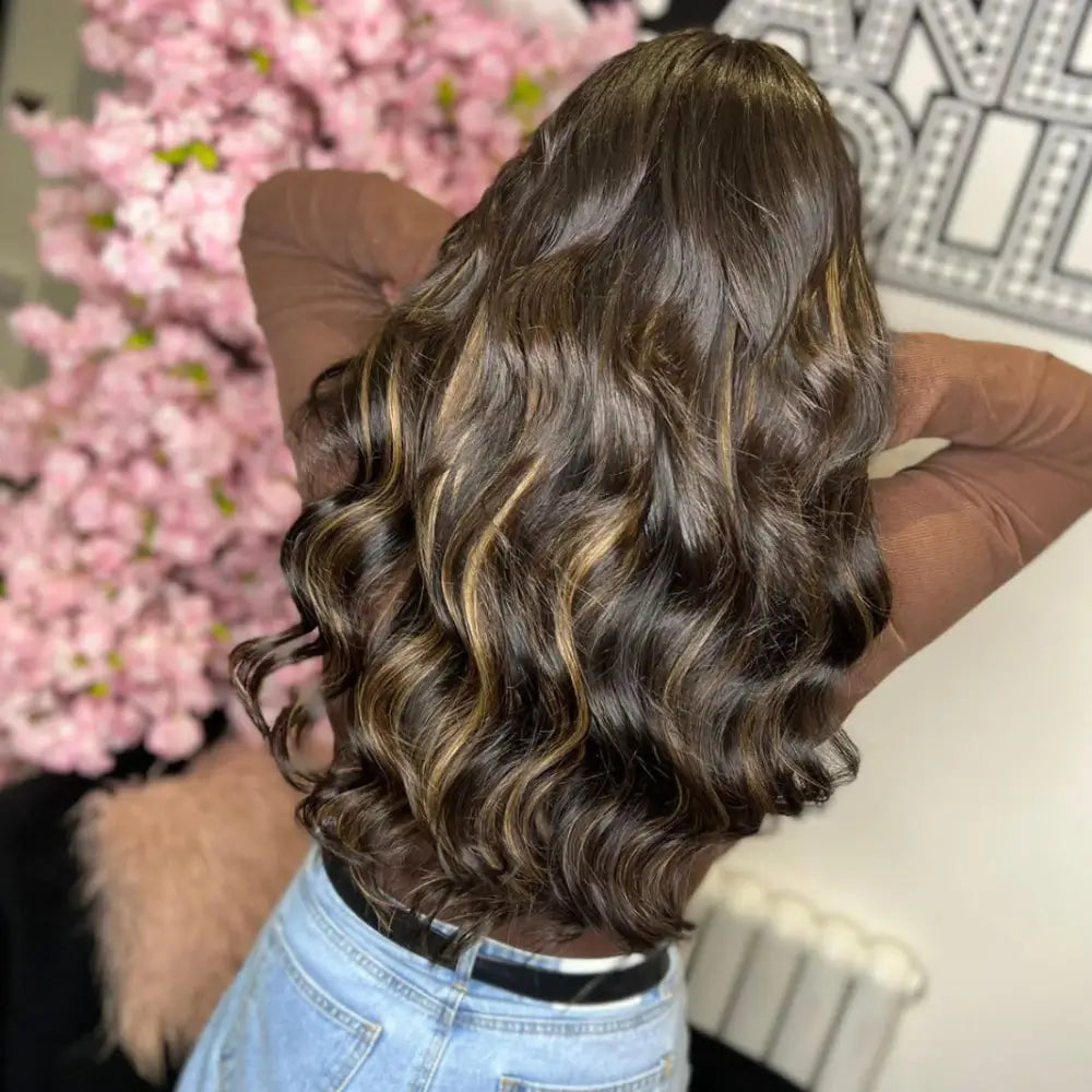 Voluminous dark brown hair with golden highlights styled in perfect bouncy curls, showcasing gdollshair extensions against pink floral backdrop.