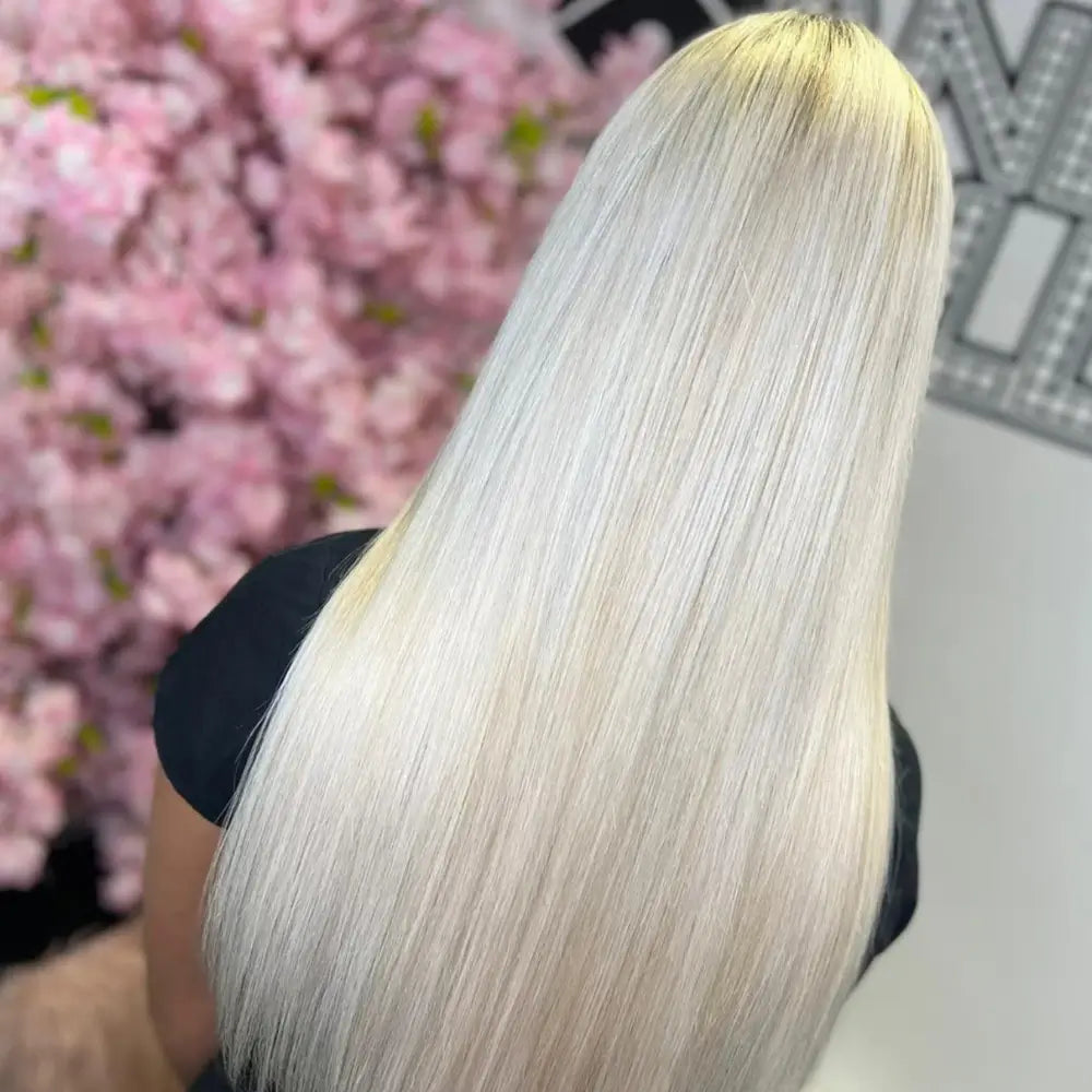 Ultra-long, sleek platinum blonde hair extensions by gdollshair creating a dramatic length transformation against pink cherry blossom backdrop.