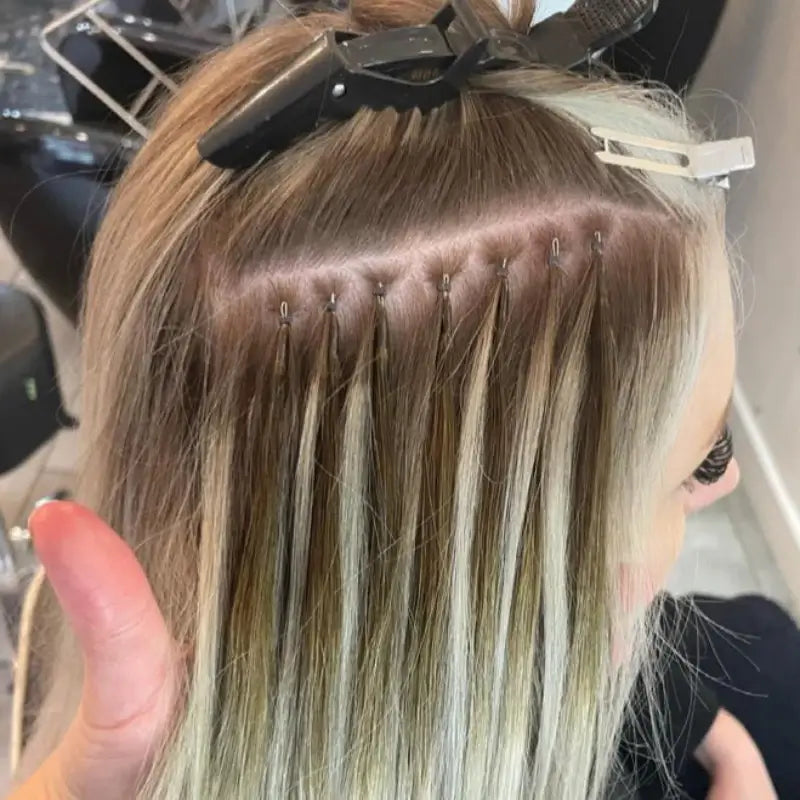 Close-up of gdollshair micro ring extension application showing precise placement of individual blonde strands with metal rings in salon.